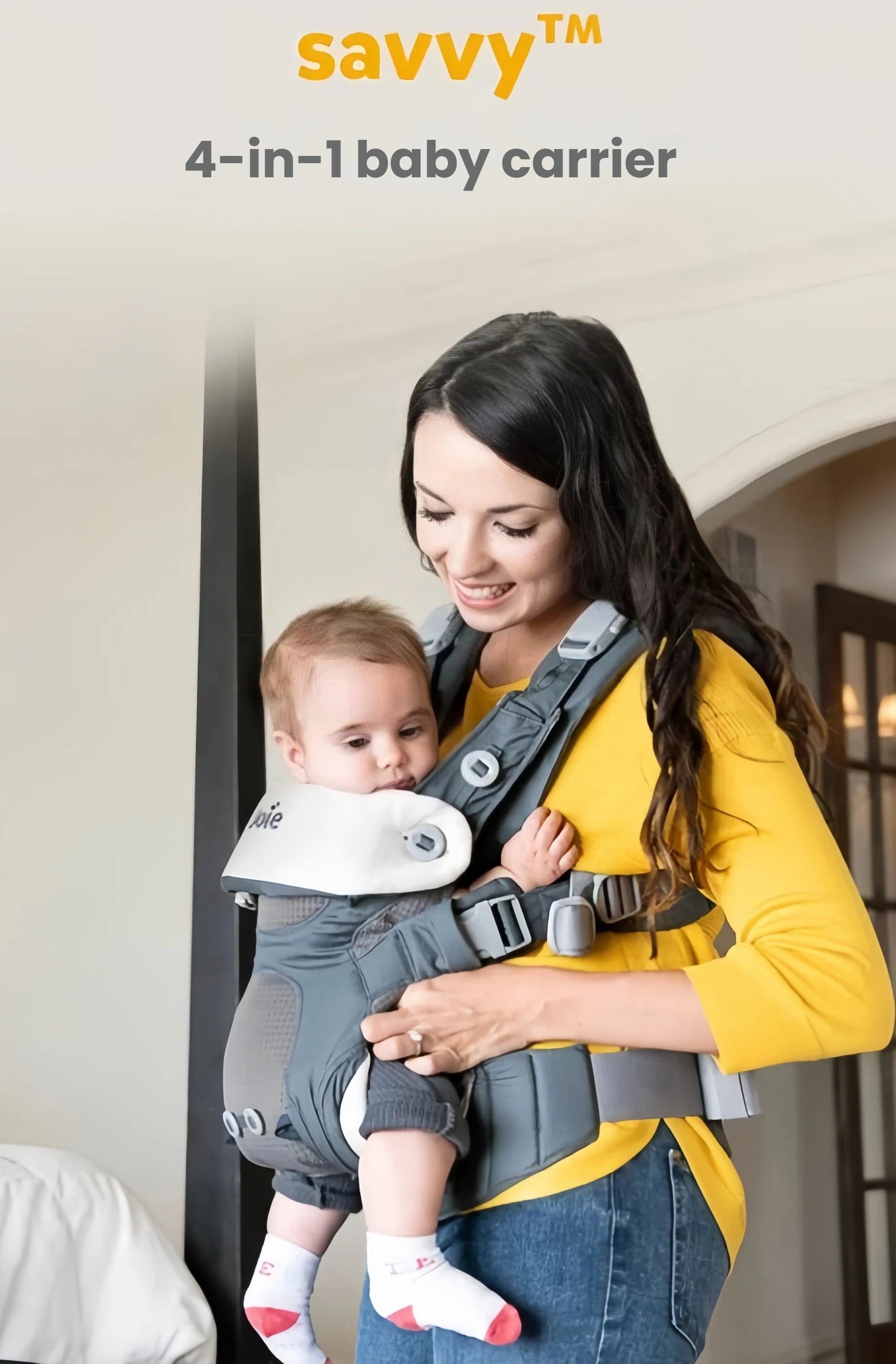 Mother carrying baby in Joie Savvy Air 4-in-1 Baby Carrier in front-facing position. The carrier supports natural bonding, includes padded headrest, and features breathable AirMesh fabric for all-day comfort.