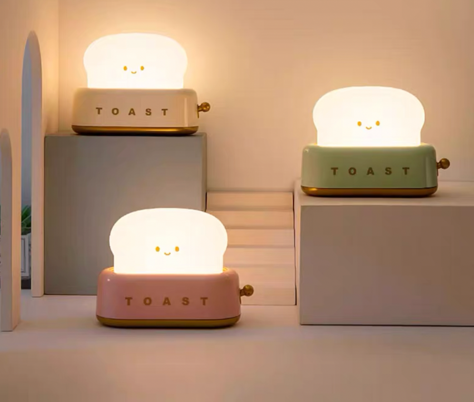 Three toaster night lights in white, green and pink on grey display plinths showing the available colour options