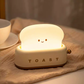 White toaster night light glowing on bedside next to teacup and saucer for cosy bedroom ambience