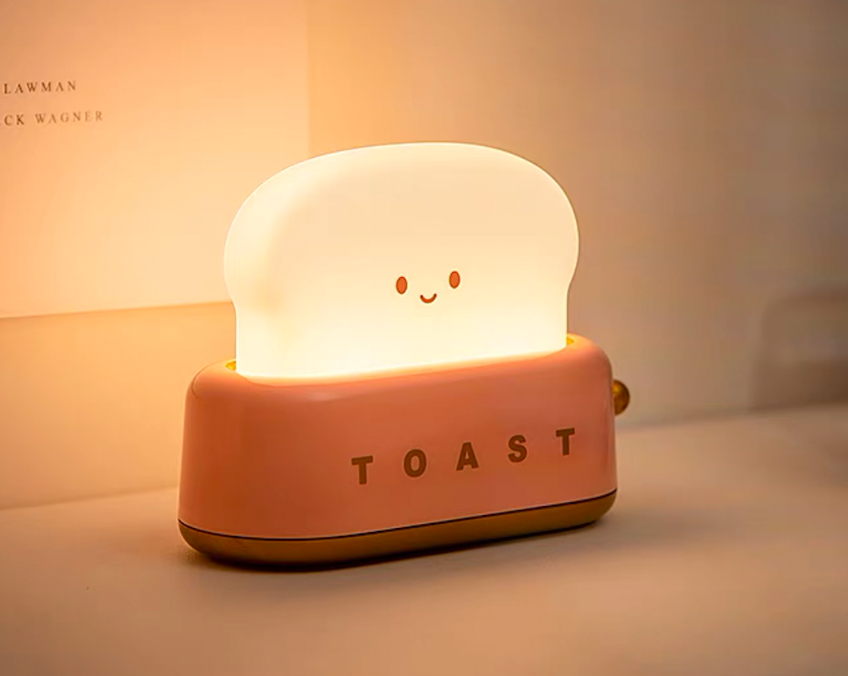 Pink toaster-shaped night light lit on desk against neutral wall showing rosy colour option and warm bedside glow