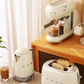 The complete Smeg 50's Style retro kitchen collection in cream, featuring the 4-slice toaster alongside the matching electric kettle and espresso coffee machine on a wooden countertop.